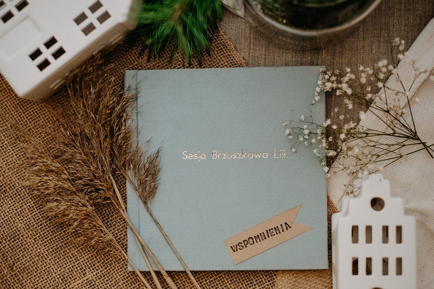 Light blue photo album titled Sesja Brzuszkowa with dried pampas grass and baby breath flowers on burlap background.