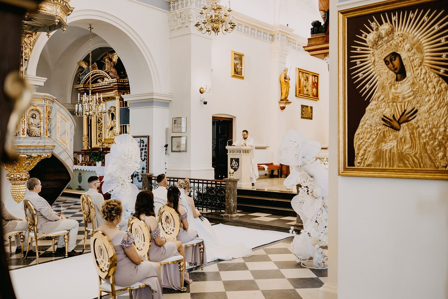 Ornate white and gold Catholic church interior during wedding ceremony with floral arch decor.