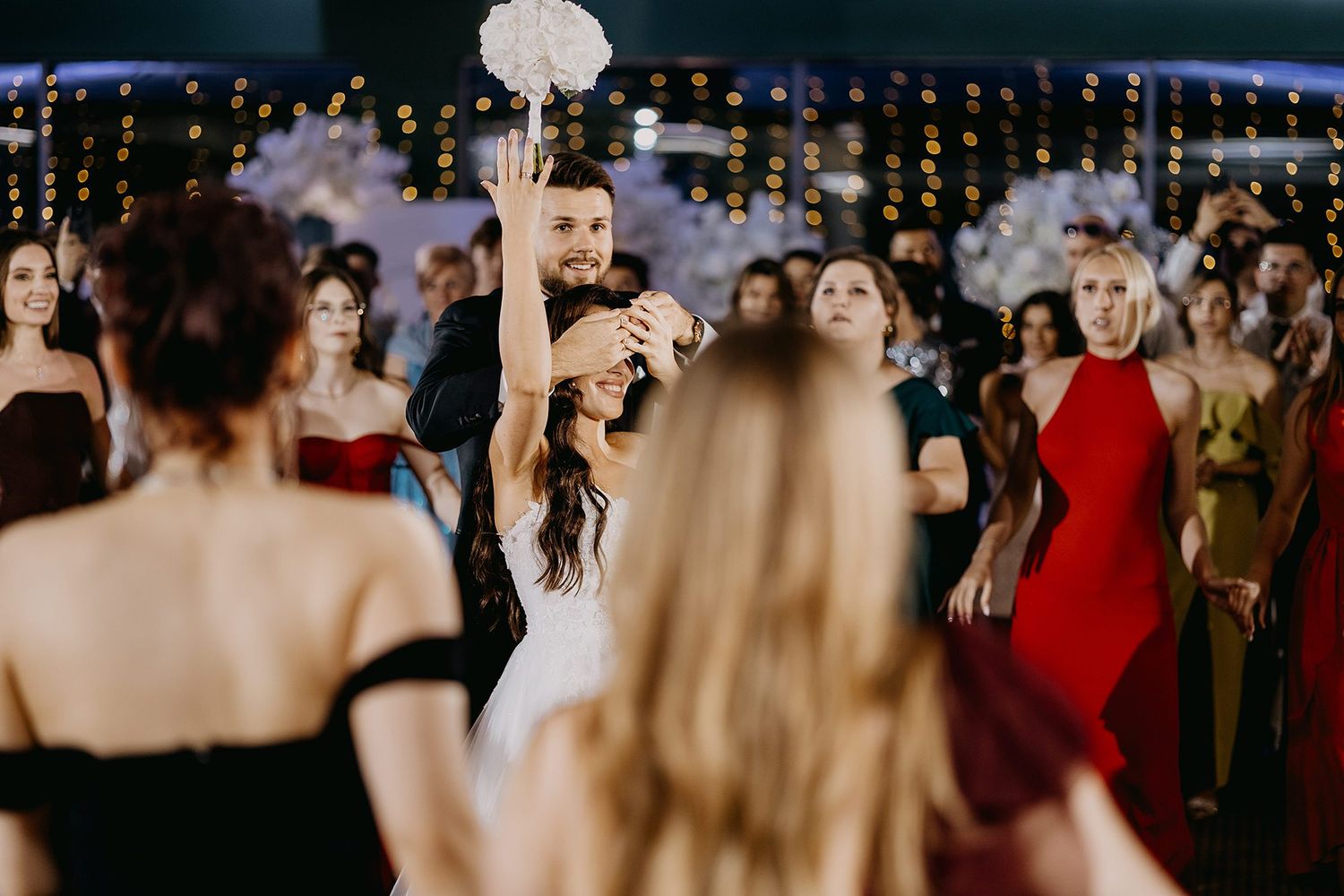Bride and groom share a joyful moment on the dance floor surrounded by elegantly dressed wedding guests.