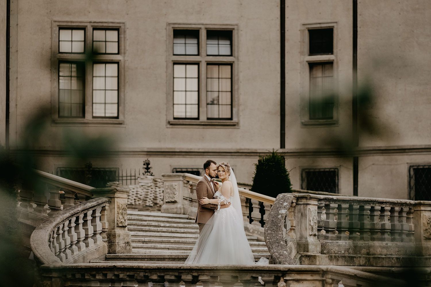 Bride and groom share a romantic moment on an ornate stone staircase of a historic manor.
