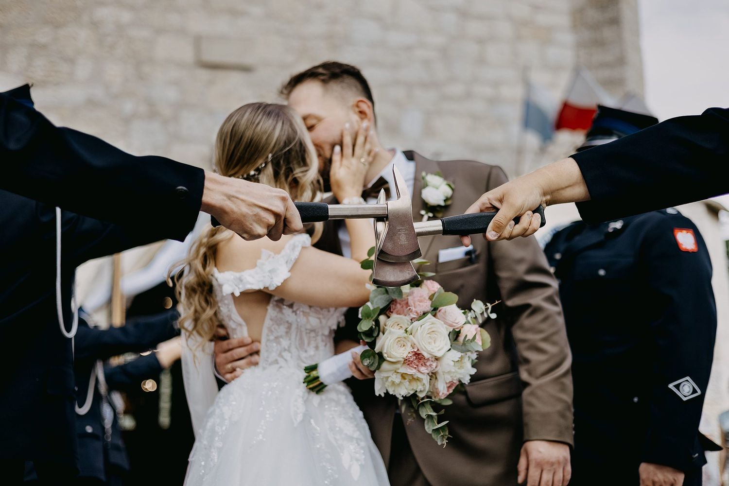 Bride and groom share a kiss under crossed swords at an outdoor military wedding ceremony.
