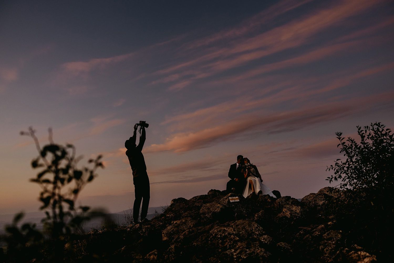 Silhouettes of photographers shooting against a dramatic colorful sunset sky on rocky terrain.
