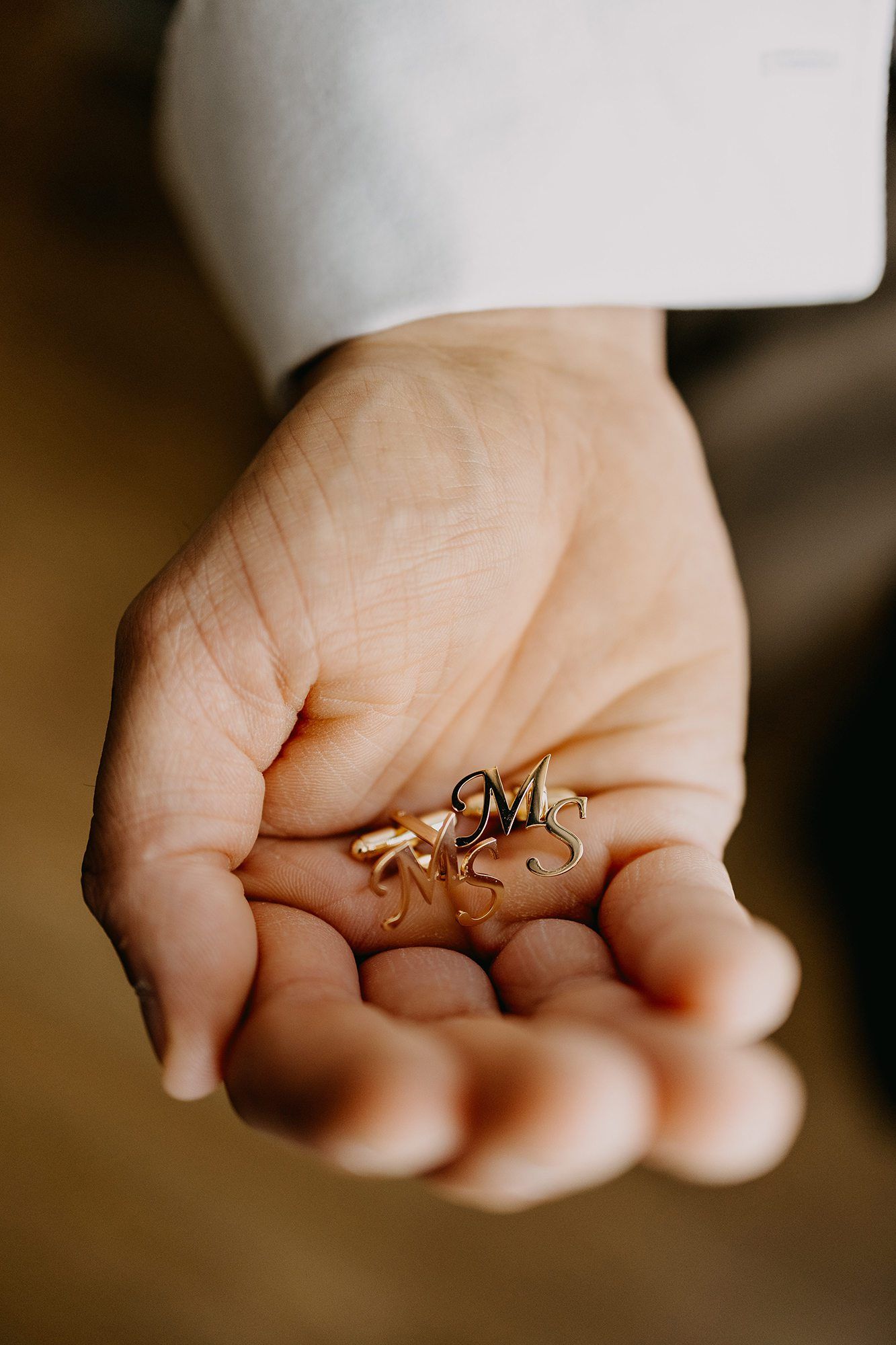 Groom holds gold monogram MS cufflinks in palm of hand before wedding ceremony.