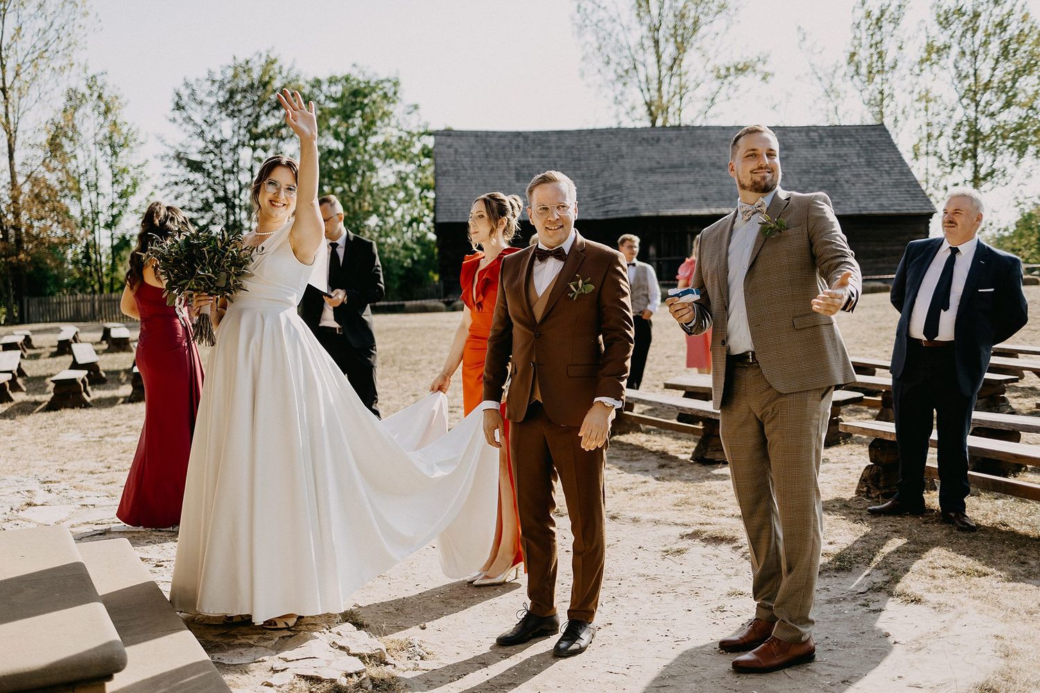 Bride and groom celebrating with wedding party outdoors at rustic venue on sunny day.