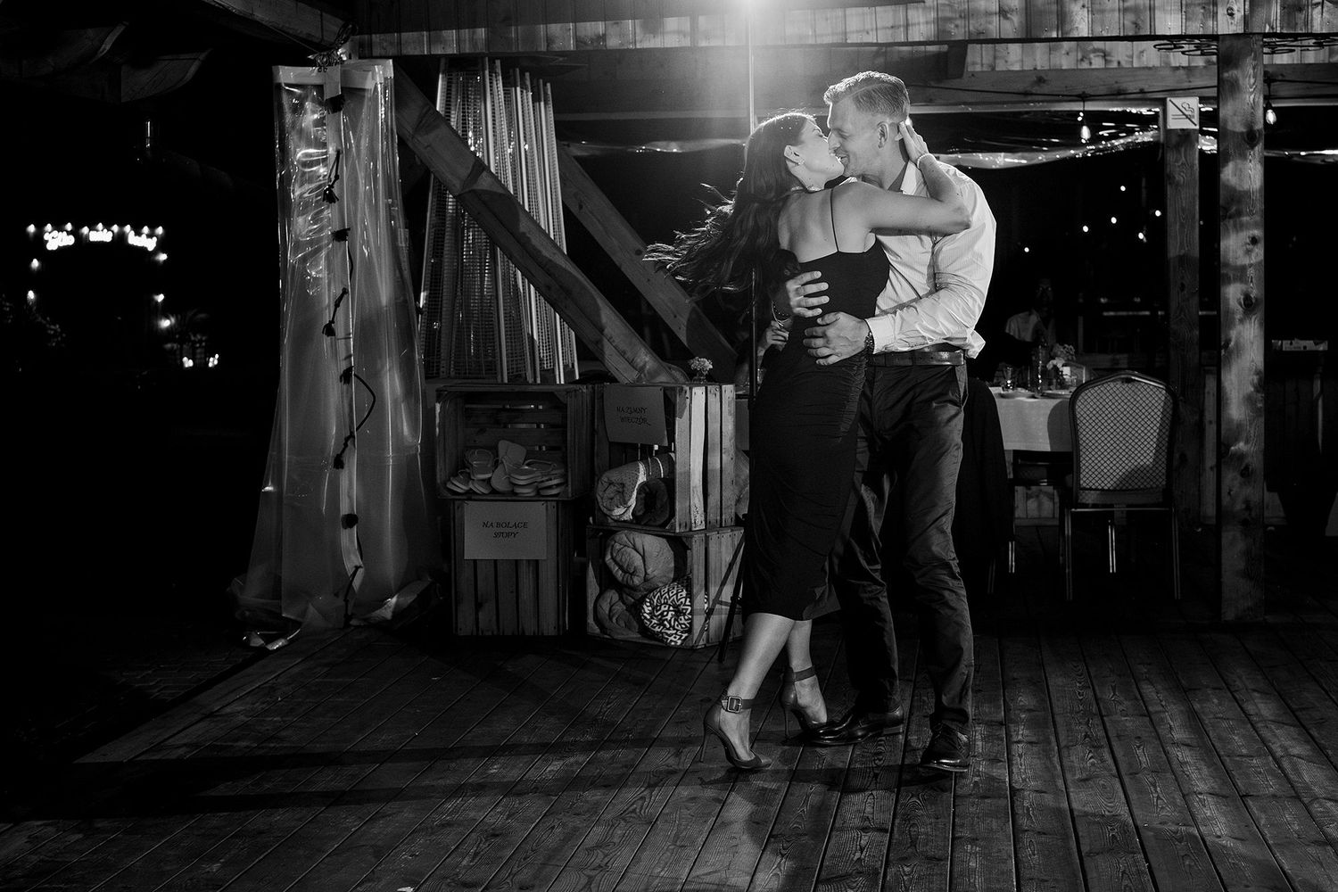 A romantic black and white photo of a couple sharing a passionate dance in a rustic wooden barn venue.