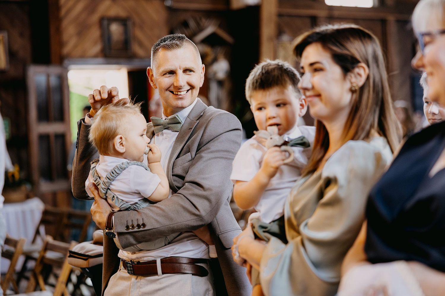 Man in gray suit holding baby while woman holds toddler during church ceremony.