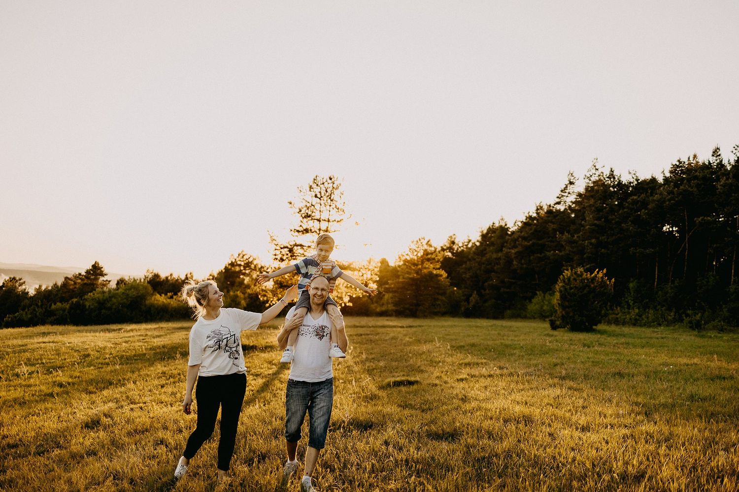 Happy family with child on shoulders walks through a golden sunlit open field.