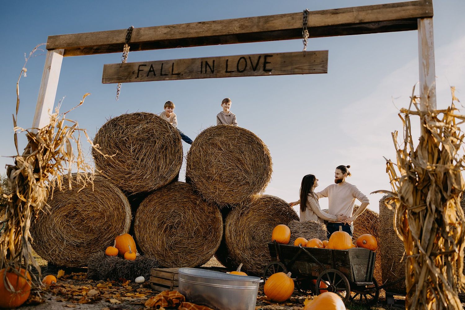 Family posing at a fall pumpkin patch with hay bales under a Fall in Love wooden sign.