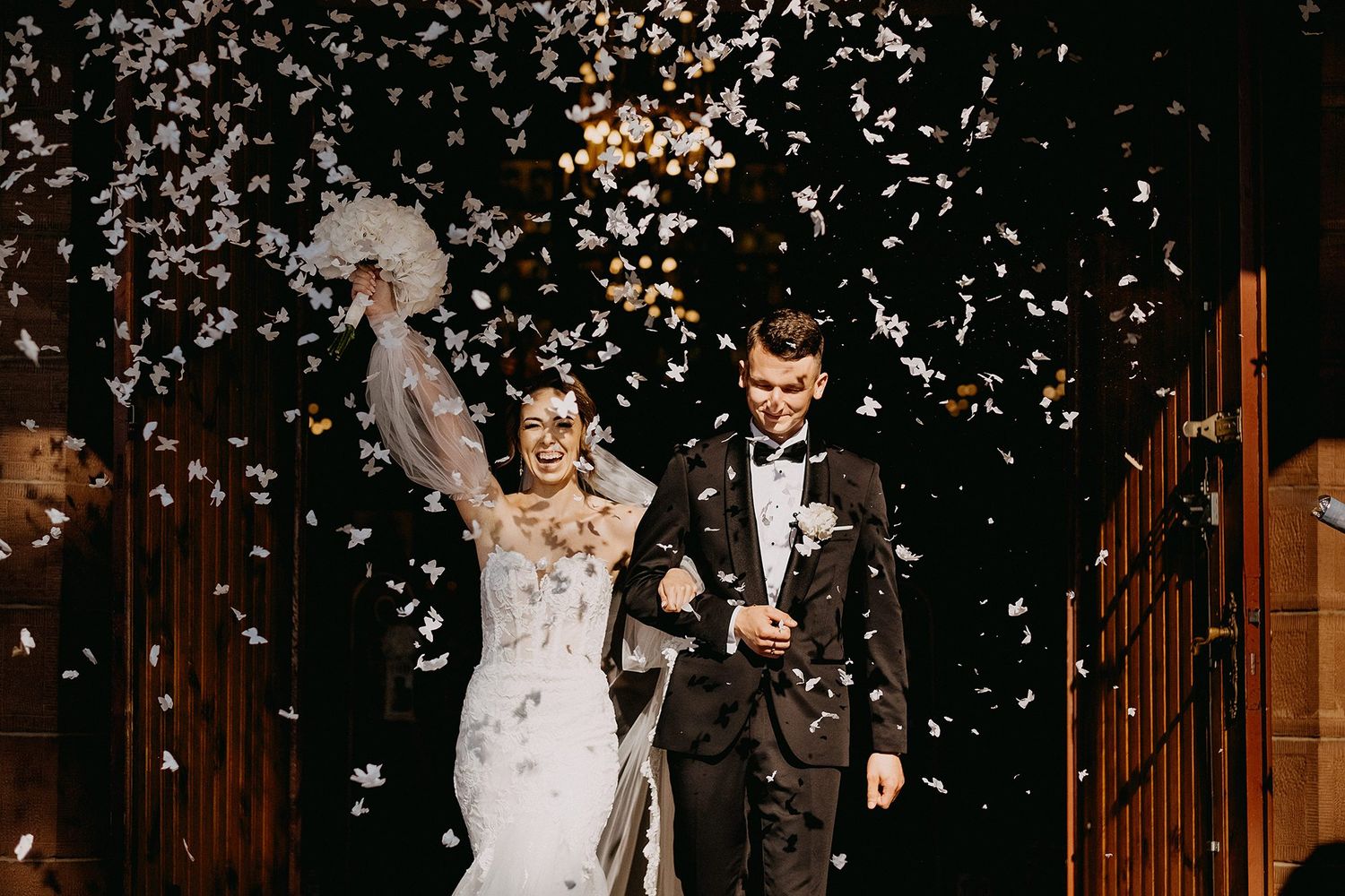 Bride and groom exit church amid confetti shower, celebrating their wedding ceremony.