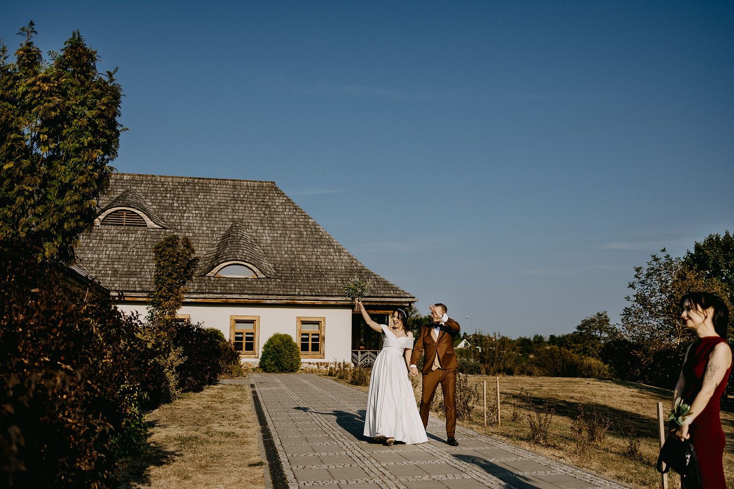 Bride and groom holding hands outside rustic thatched roof wedding venue.
