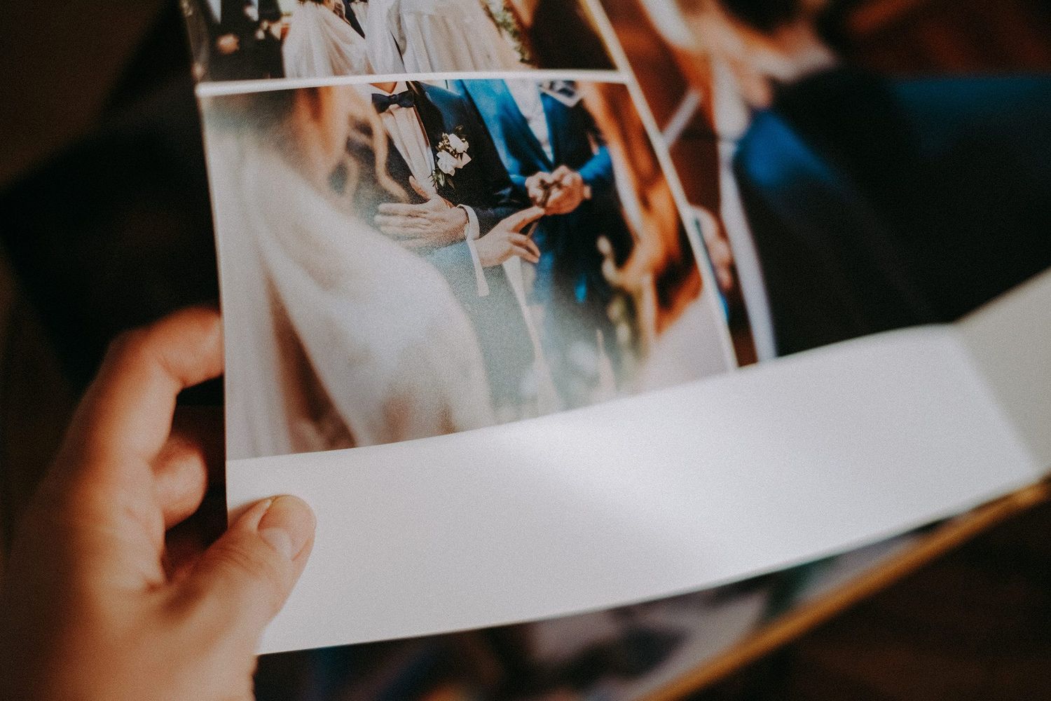 Close-up of hands holding open wedding photo album page showing elegant ceremony and celebration photographs.