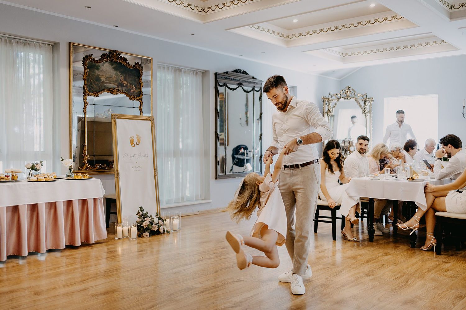 Father dancing and spinning his young daughter on a wooden dance floor at a christening reception.
