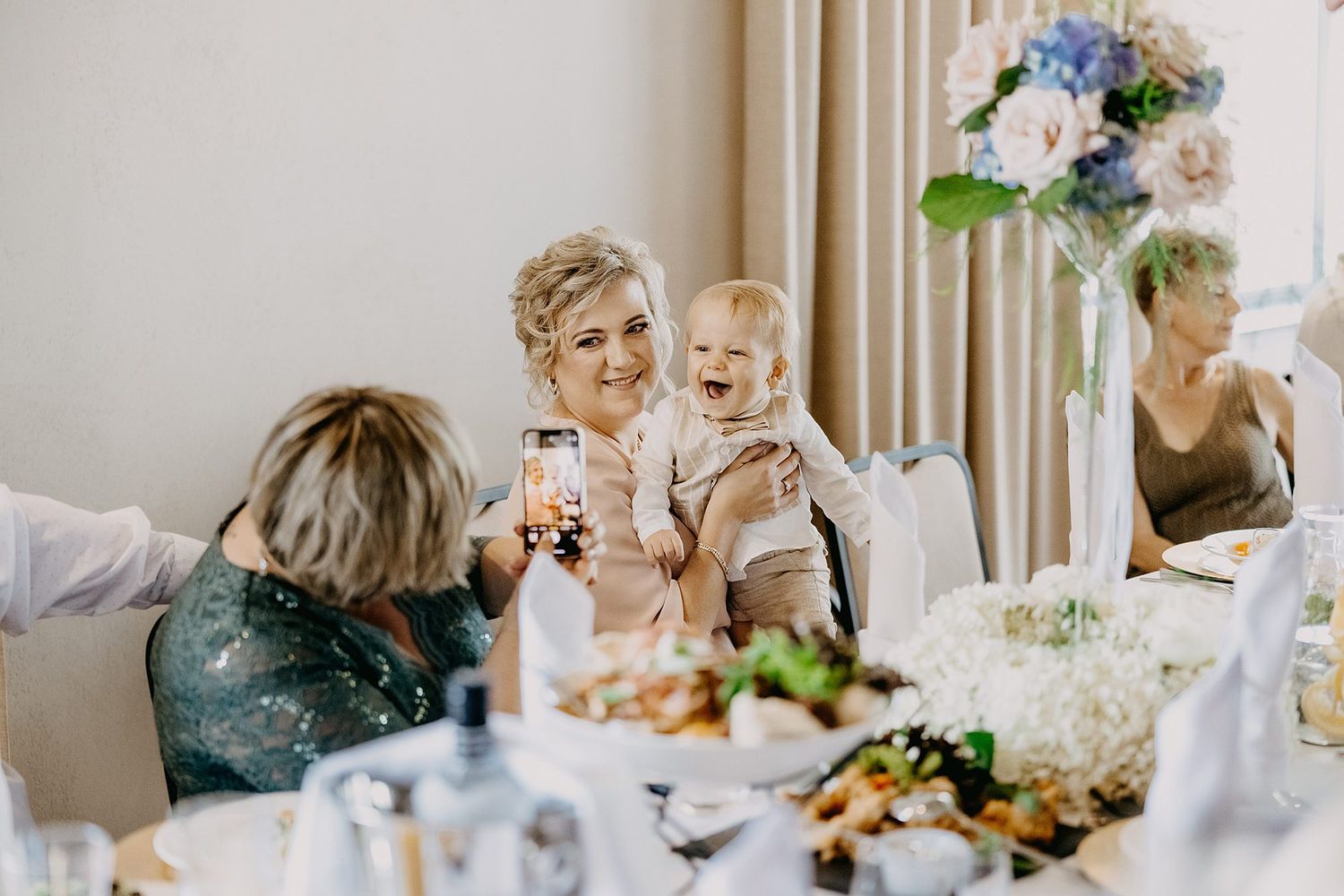 Grandmother laughing joyfully while holding a happy baby at an elegant christening reception dinner.