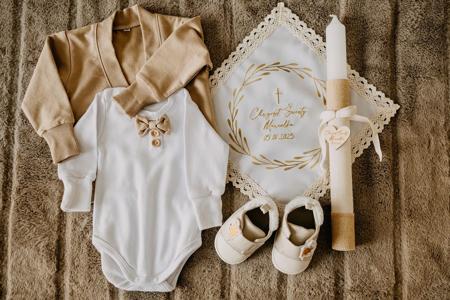 Baby christening outfit with white bodysuit, gold shoes, baptism candle and embroidered cloth.