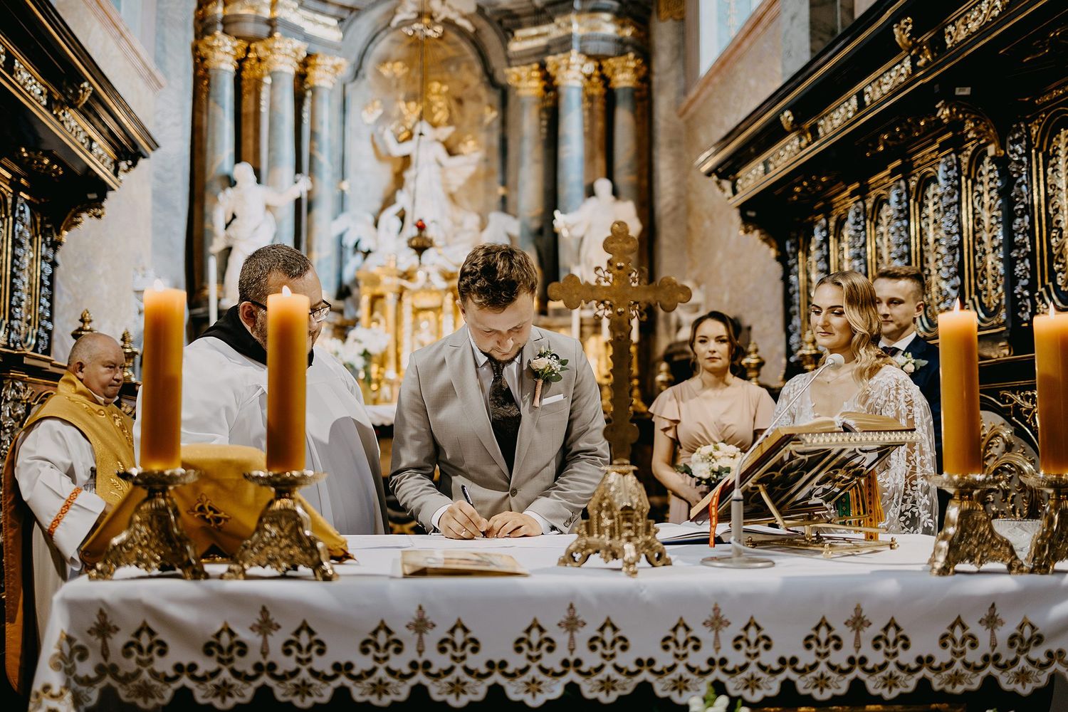 Groom signing the wedding register at an ornate golden altar in a historic baroque church.