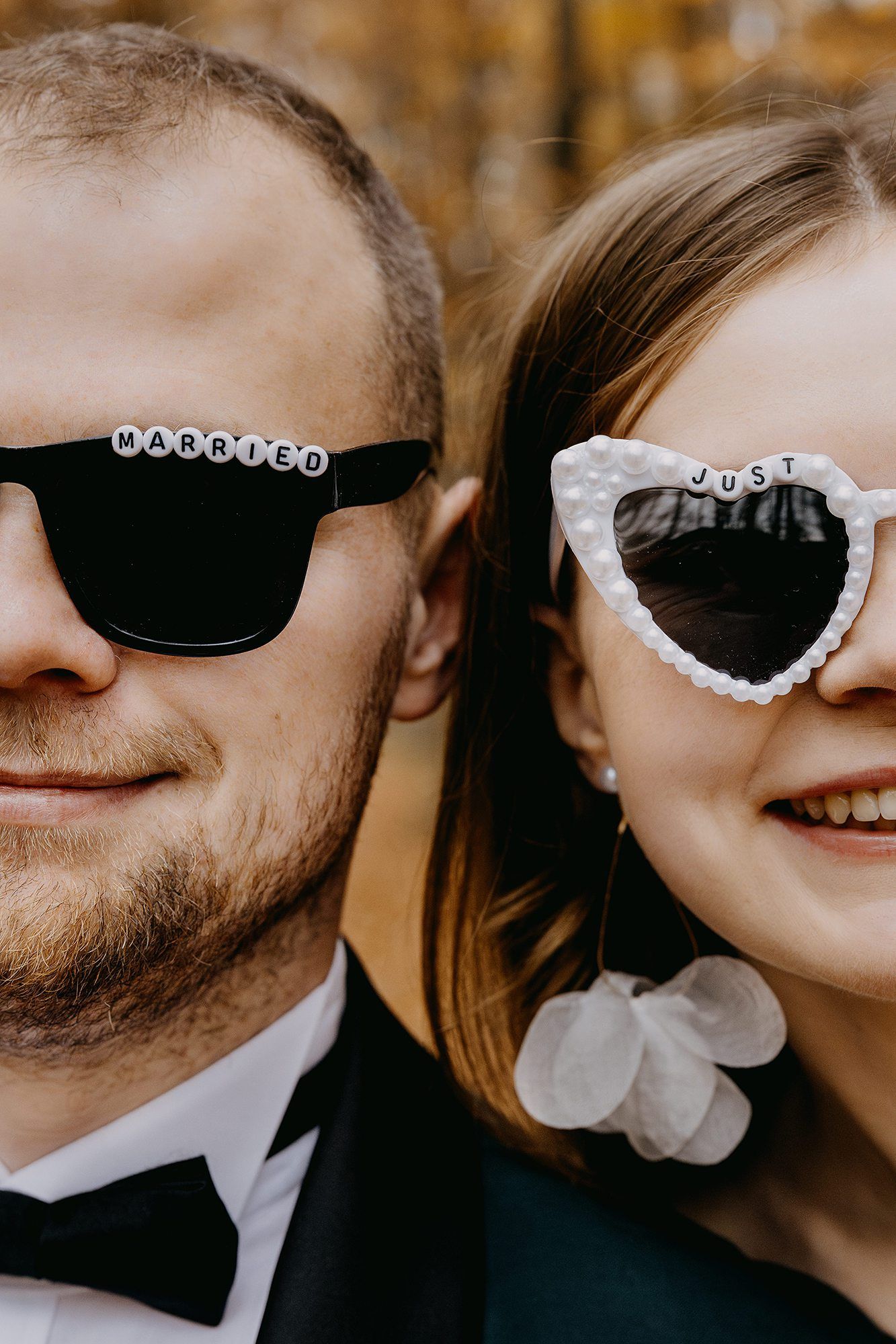 Newlyweds wear fun sunglasses reading MARRIED and JUST in golden autumn outdoor setting.
