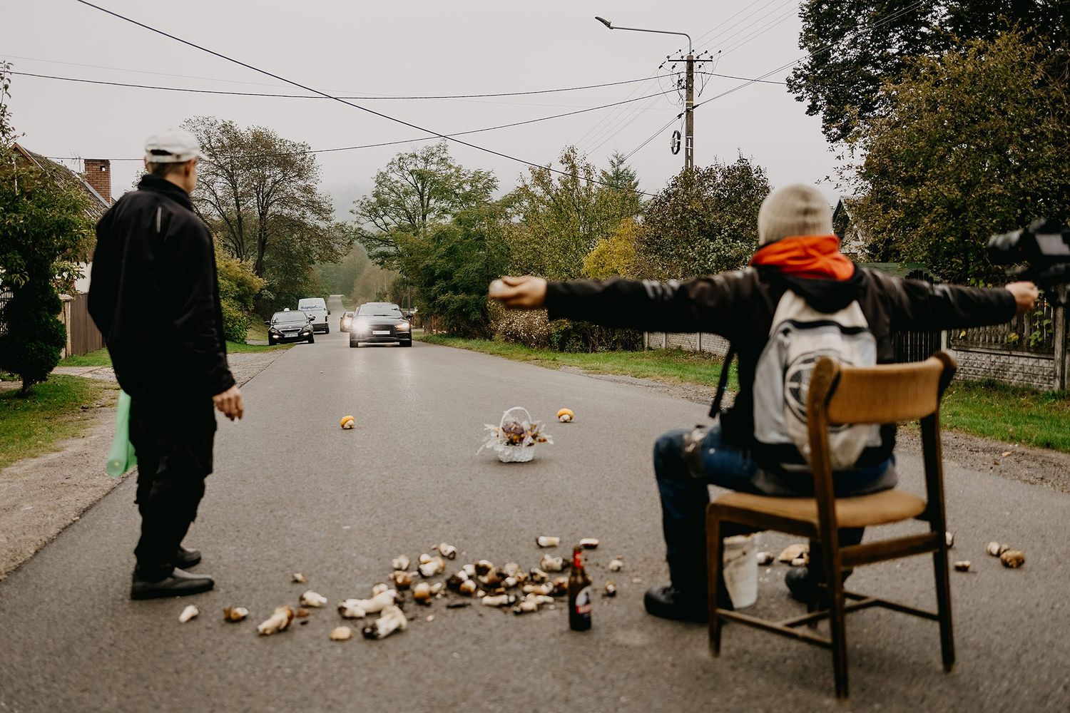 Person sitting on a chair in a rainy street with arms outstretched near scattered items.