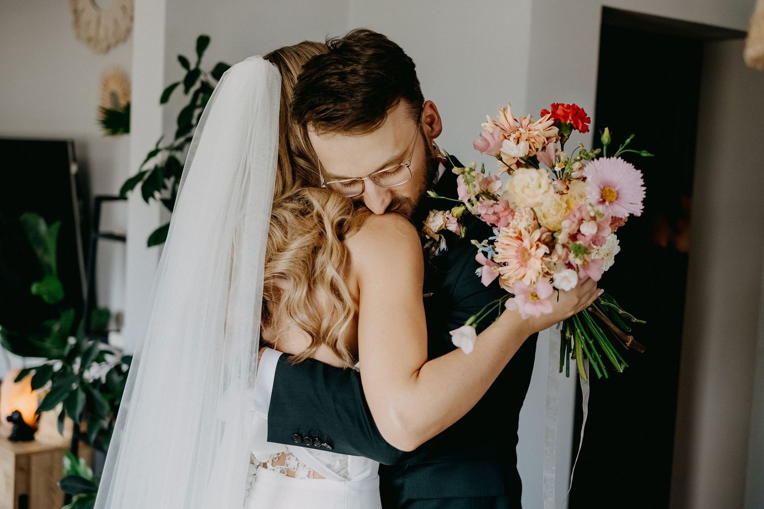 A bride and groom share a tender embrace, with the bride holding a pastel floral bouquet on their wedding day.