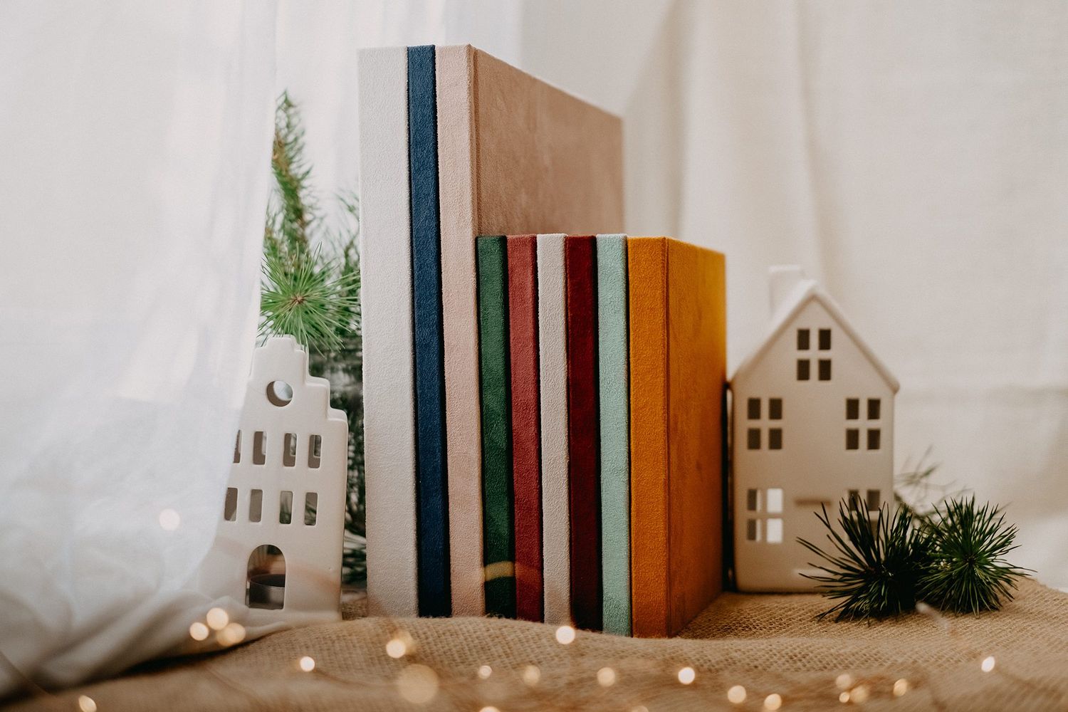 Colorful stack of books between two white ceramic house bookends with festive holiday decor.