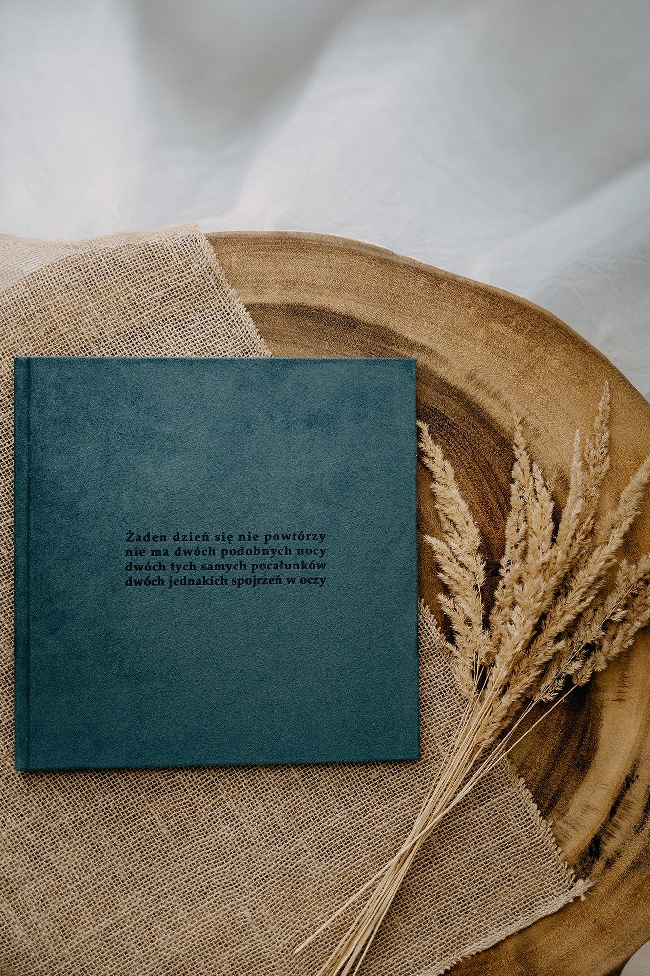 Teal velvet photo album with Polish text quote on burlap beside dried wheat stalks.