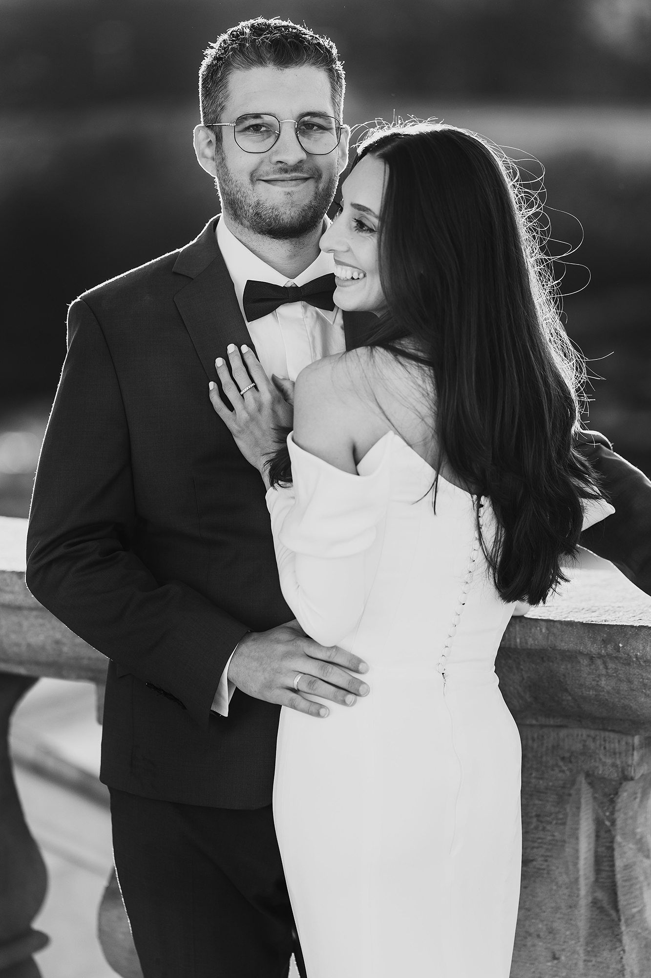 Black and white portrait of bride and groom embracing near a balustrade.