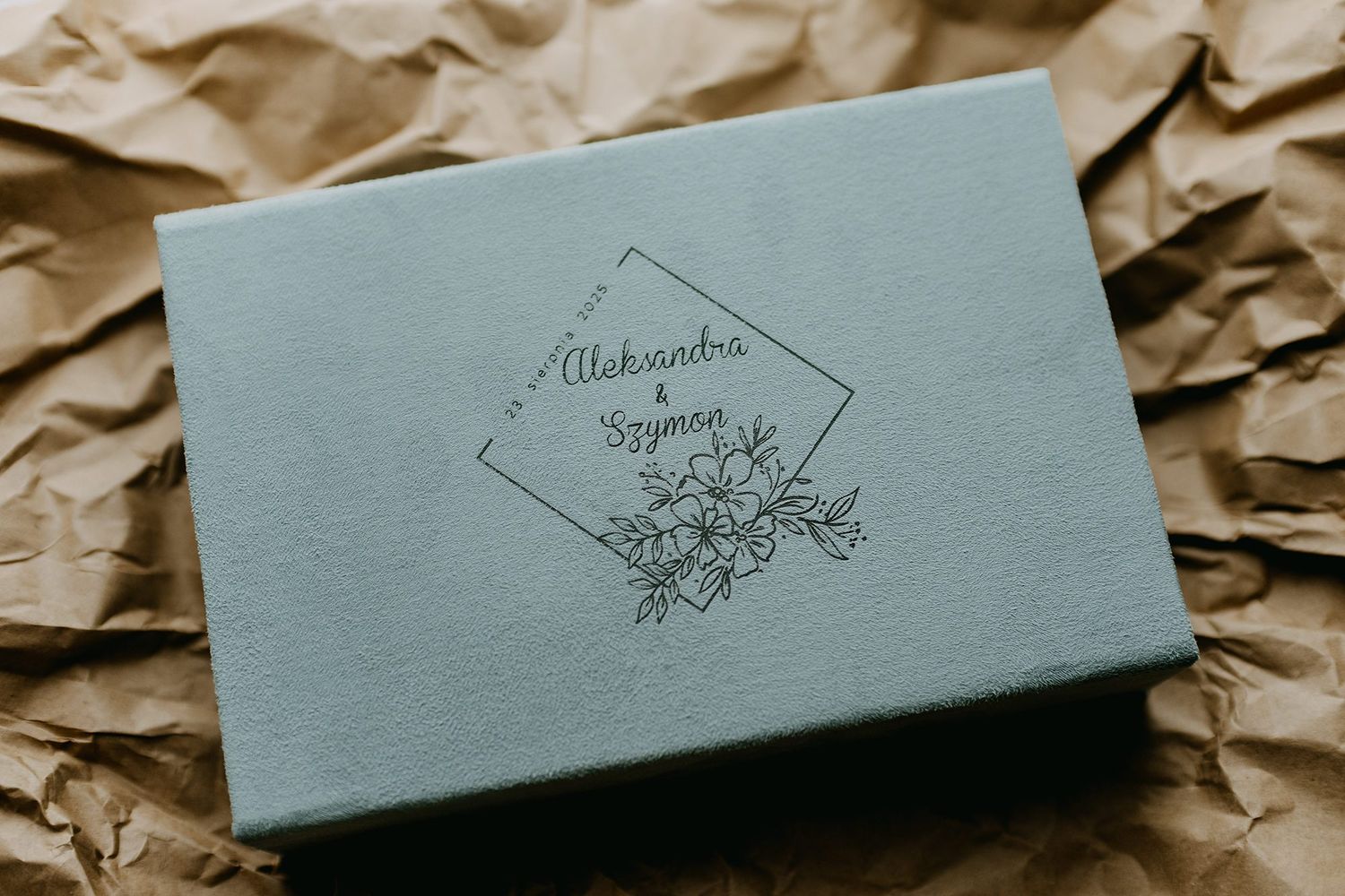 Sage green linen wedding box with floral engraving reading Aleksandra i Szymon on kraft paper.