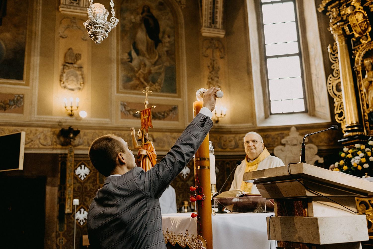 A priest raises a chalice during a Catholic Mass ceremony in an ornate church with golden altar decorations.