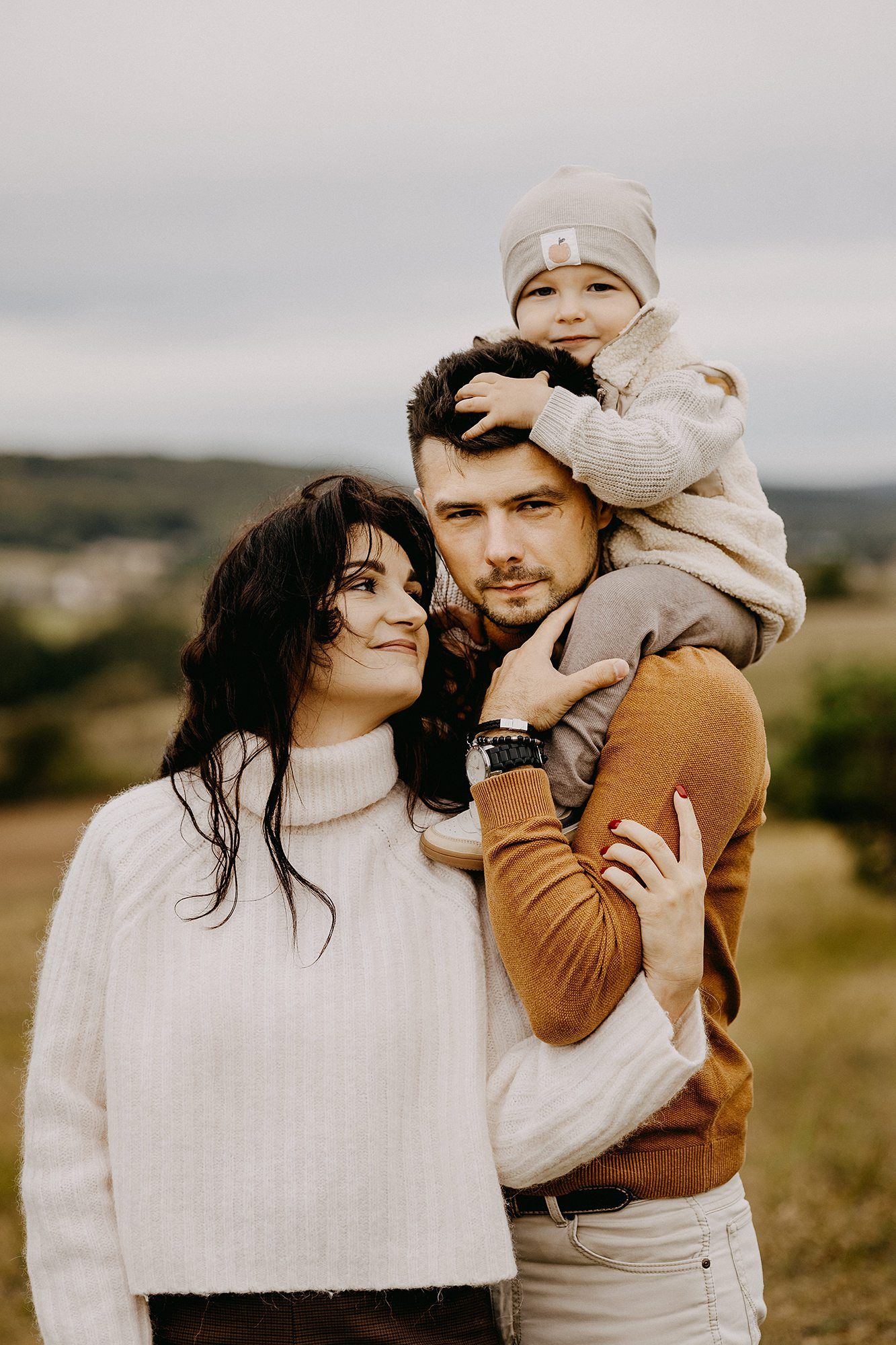 Young family with toddler on father's shoulders posing in autumn field.