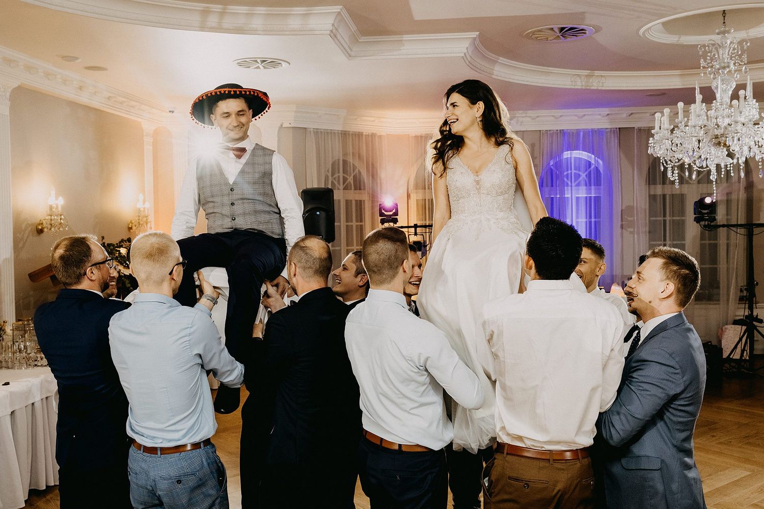 Bride and groom lifted by groomsmen during lively wedding reception celebration.
