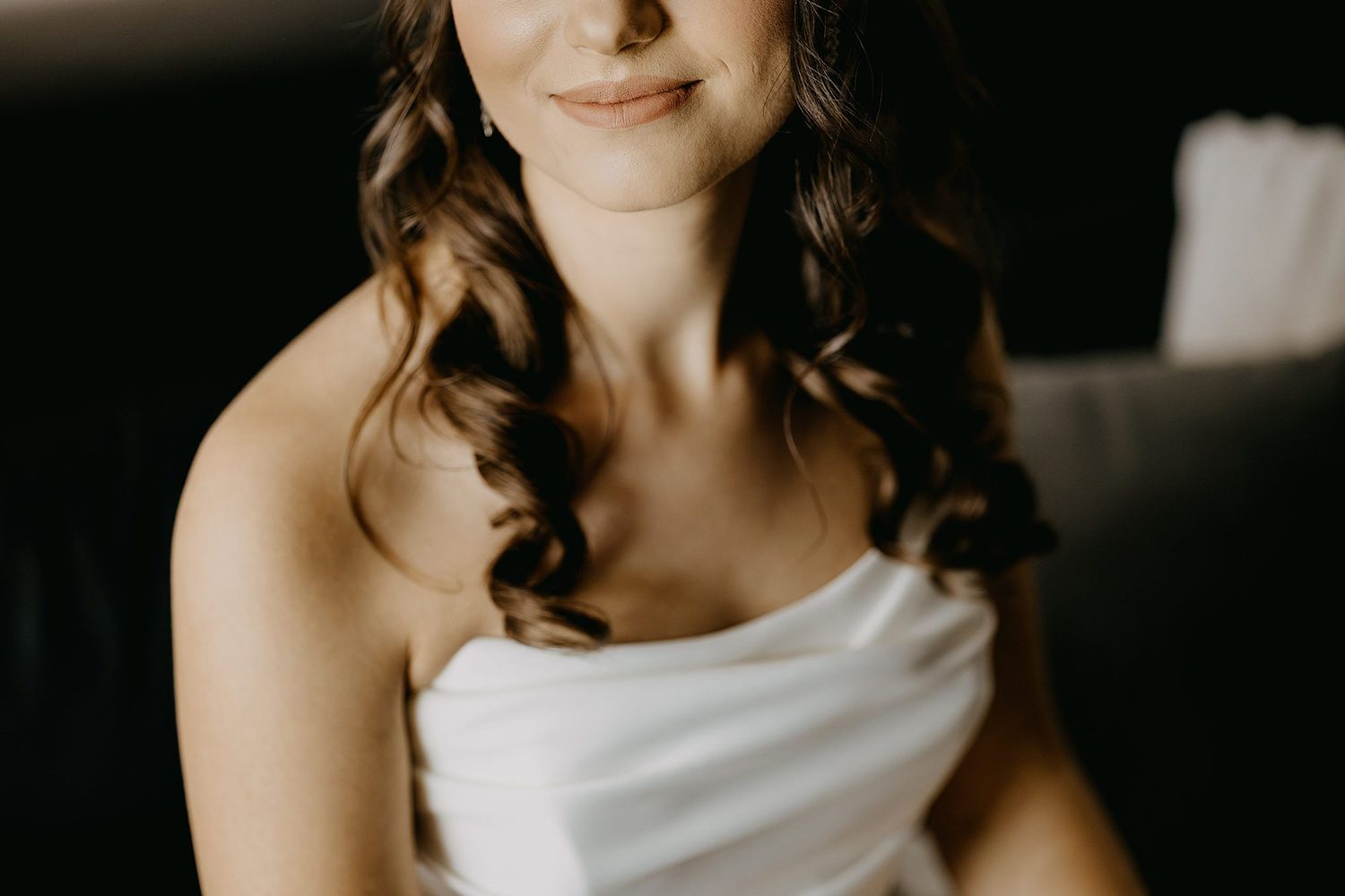 Beautiful bride in white strapless dress with soft curled hair smiling softly.