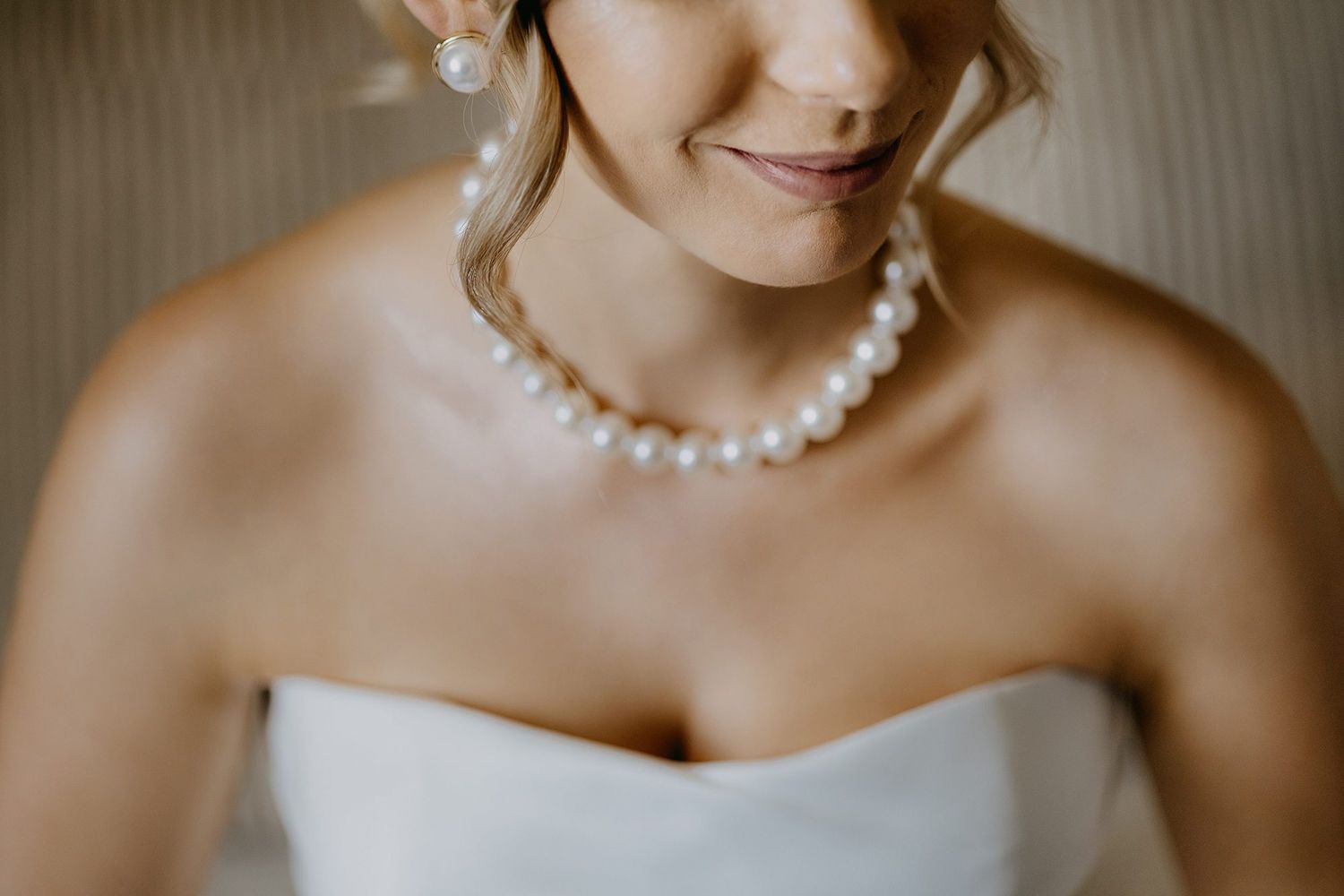 Close-up of bride wearing classic pearl necklace and earrings with strapless white wedding gown.