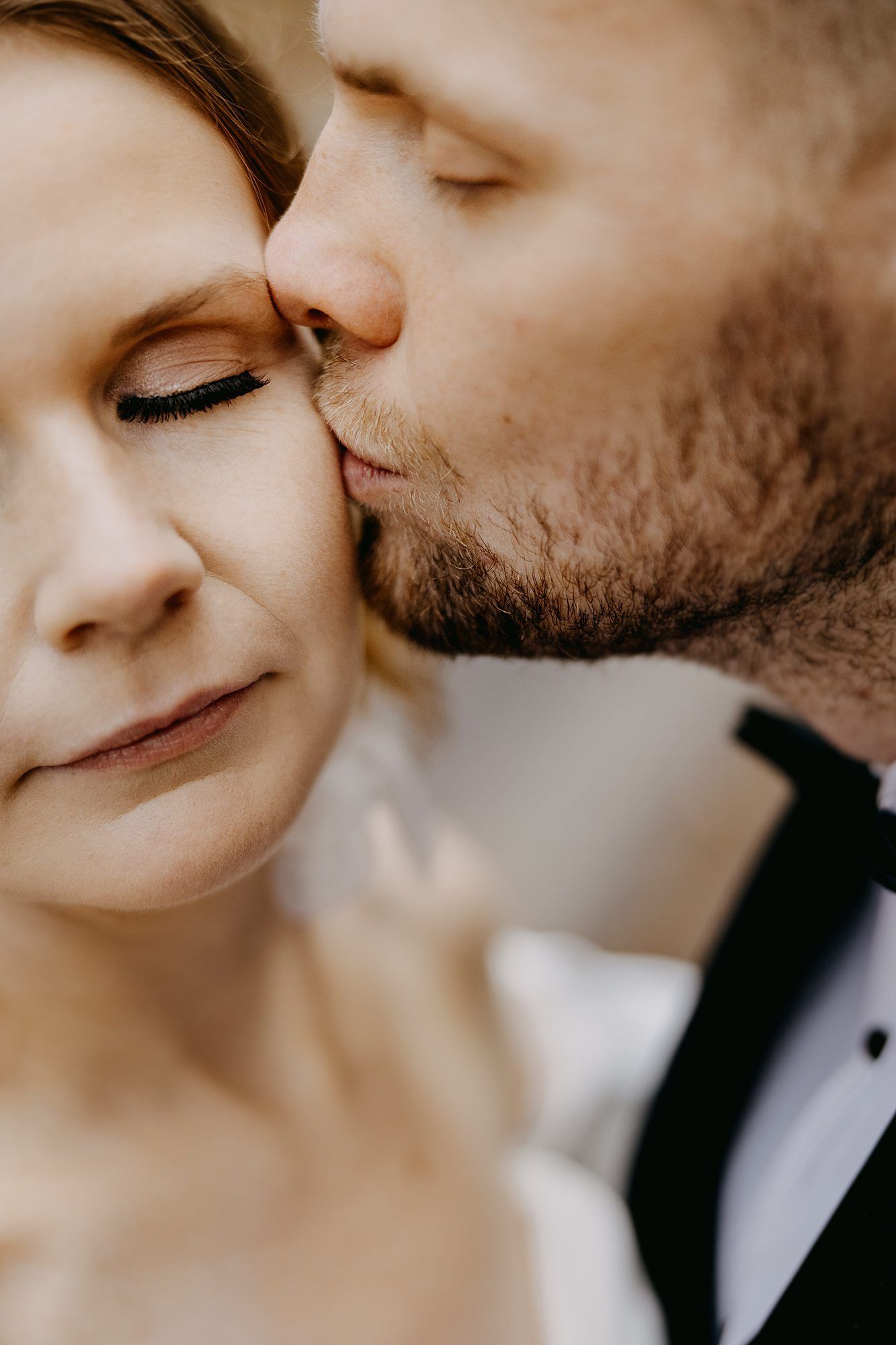 Groom tenderly kisses bride on the cheek in a close-up intimate wedding portrait.