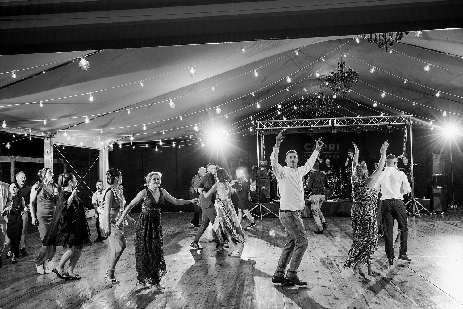Black and white photo of wedding guests energetically dancing in a festive reception hall.