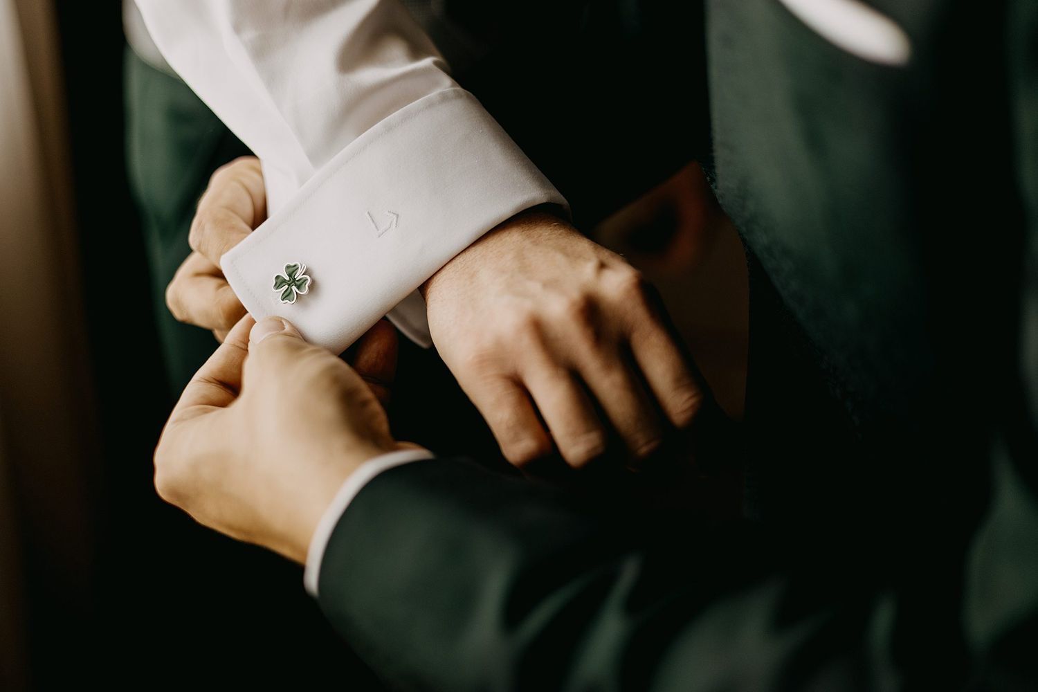 Close-up of groom having elegant crystal cufflinks fastened on white dress shirt sleeve.