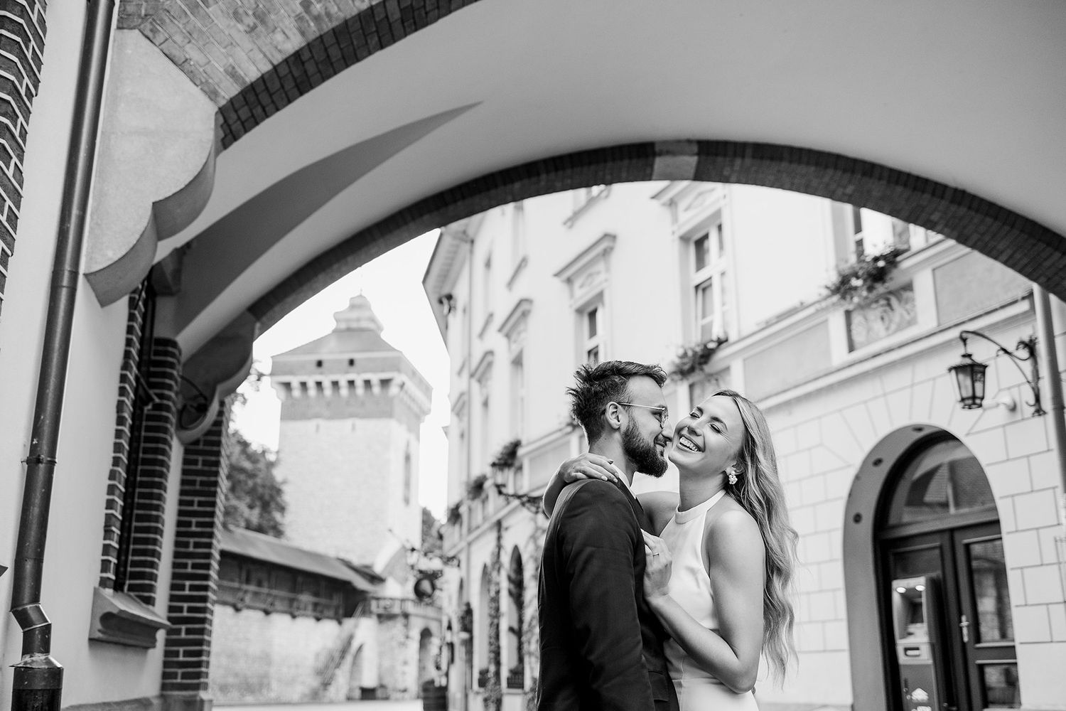 Couple sharing romantic moment under stone arch in black and white wedding photo.