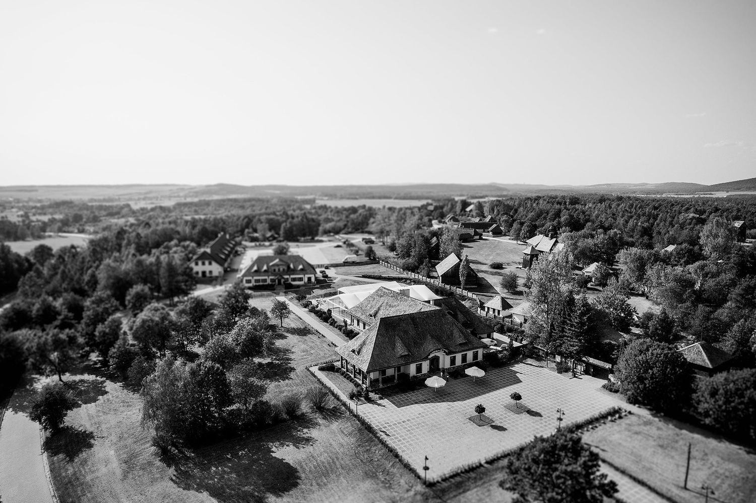 Aerial black and white photo of a rural estate surrounded by lush trees and open fields in the countryside.