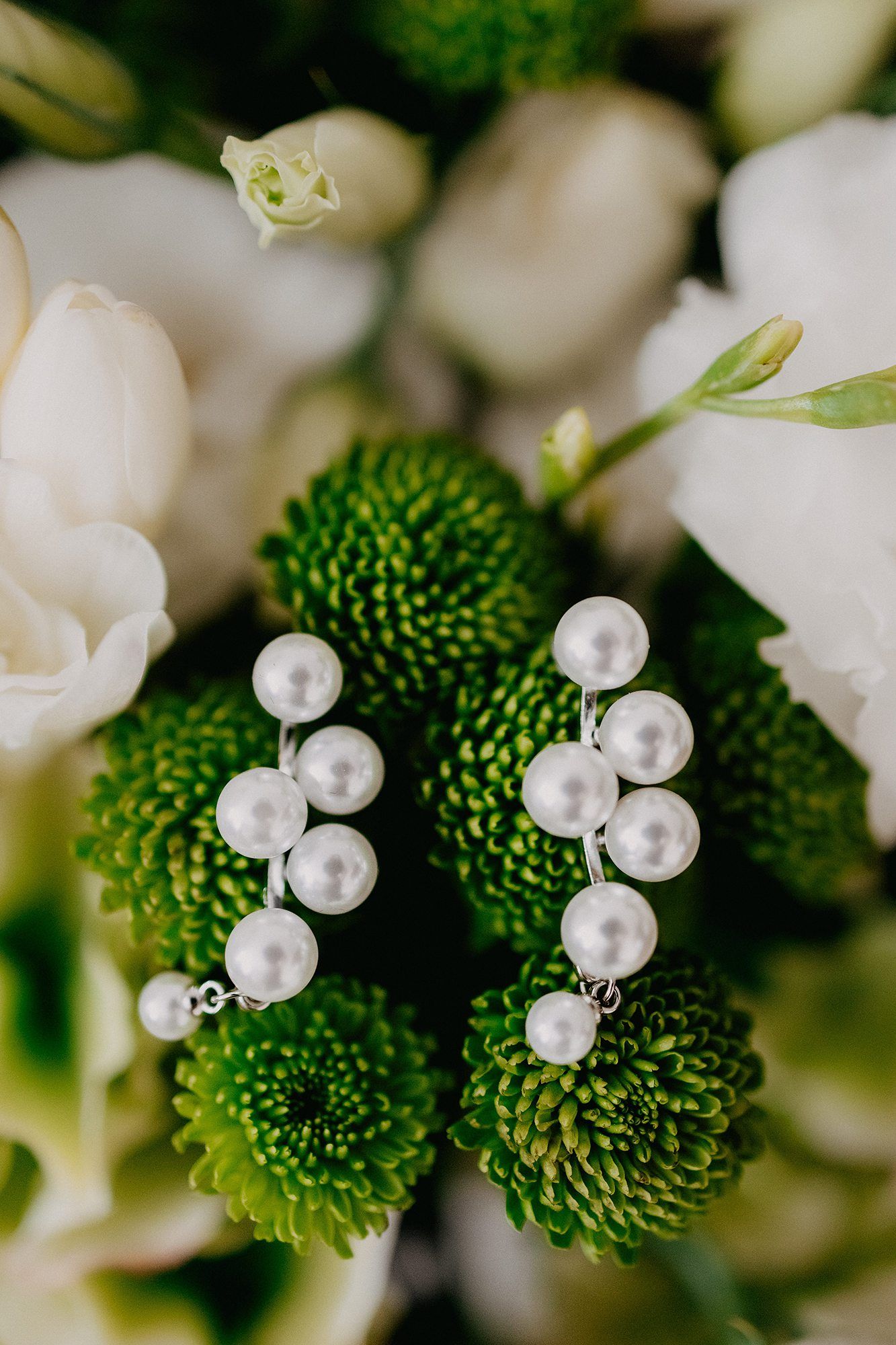 Pearl cluster earrings resting on green chrysanthemum flowers with white roses in the background.