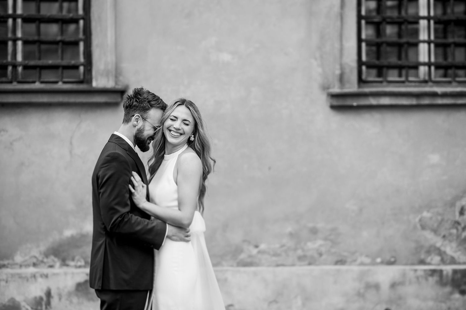 Bride and groom sharing tender embrace against aged wall in black and white photo.