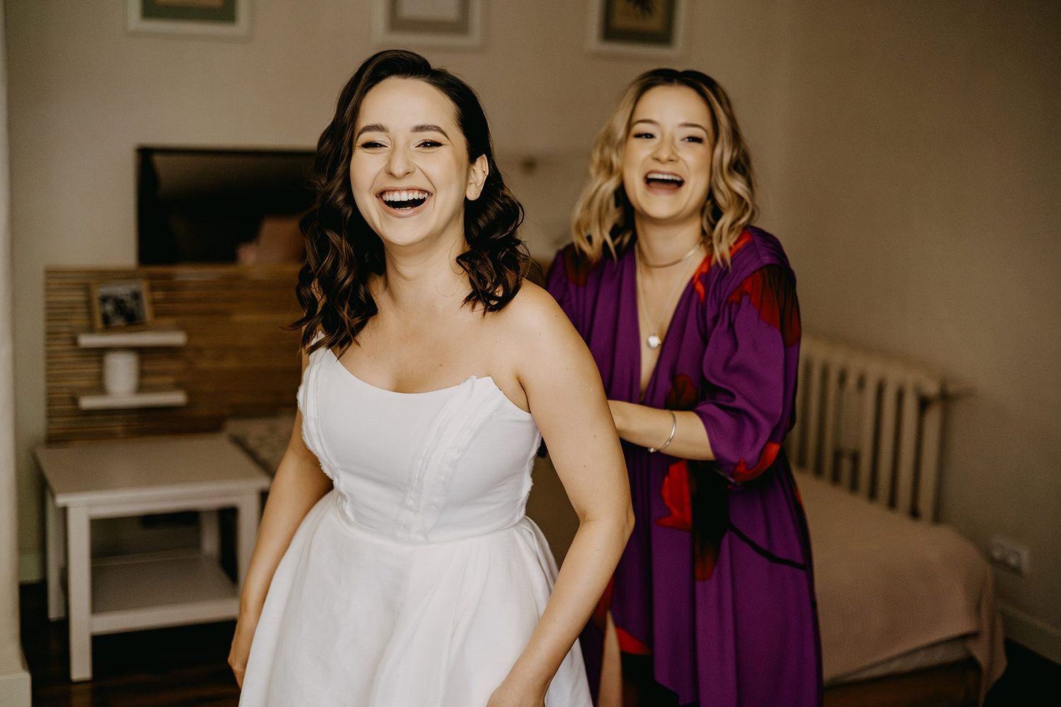 Bride and bridesmaid laughing joyfully together during wedding morning preparations.