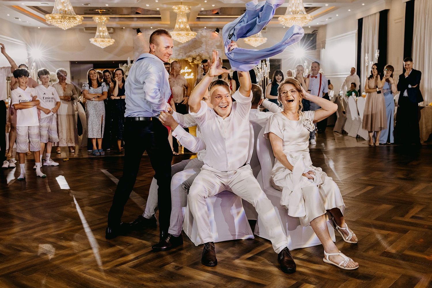 Joyful wedding reception dance floor moment with guests celebrating, bride and groom laughing in elegant ballroom.