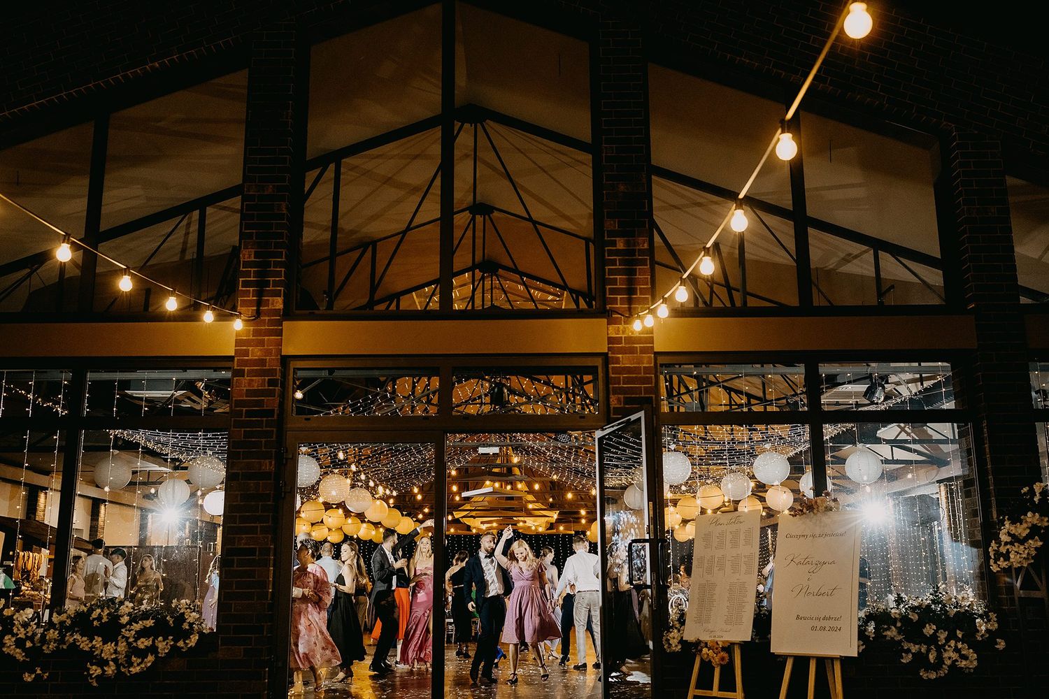 Elegant outdoor wedding reception venue with string lights, brick walls, and guests dancing at night.