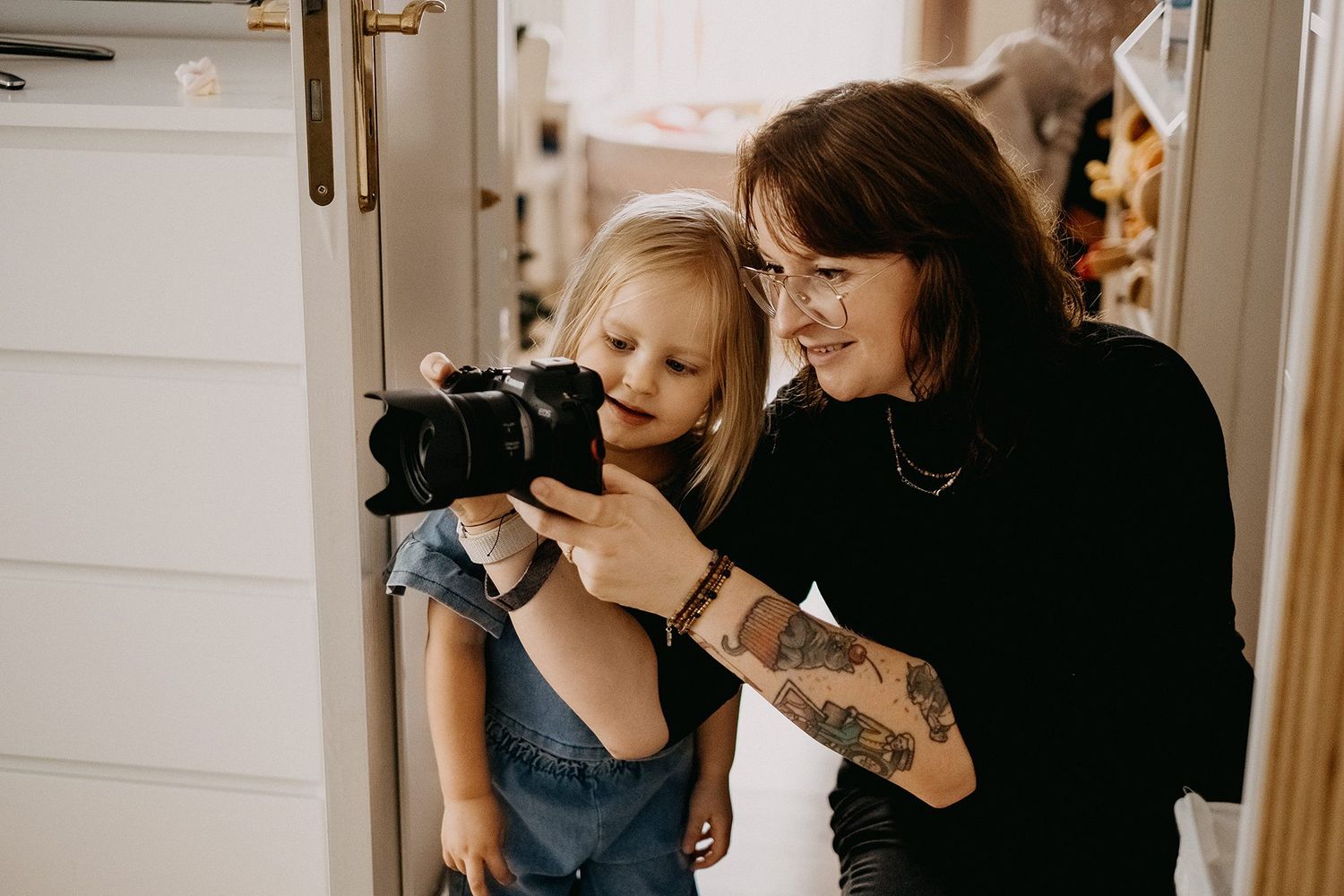 Female photographer with tattoos showing camera preview screen to curious young blonde child.