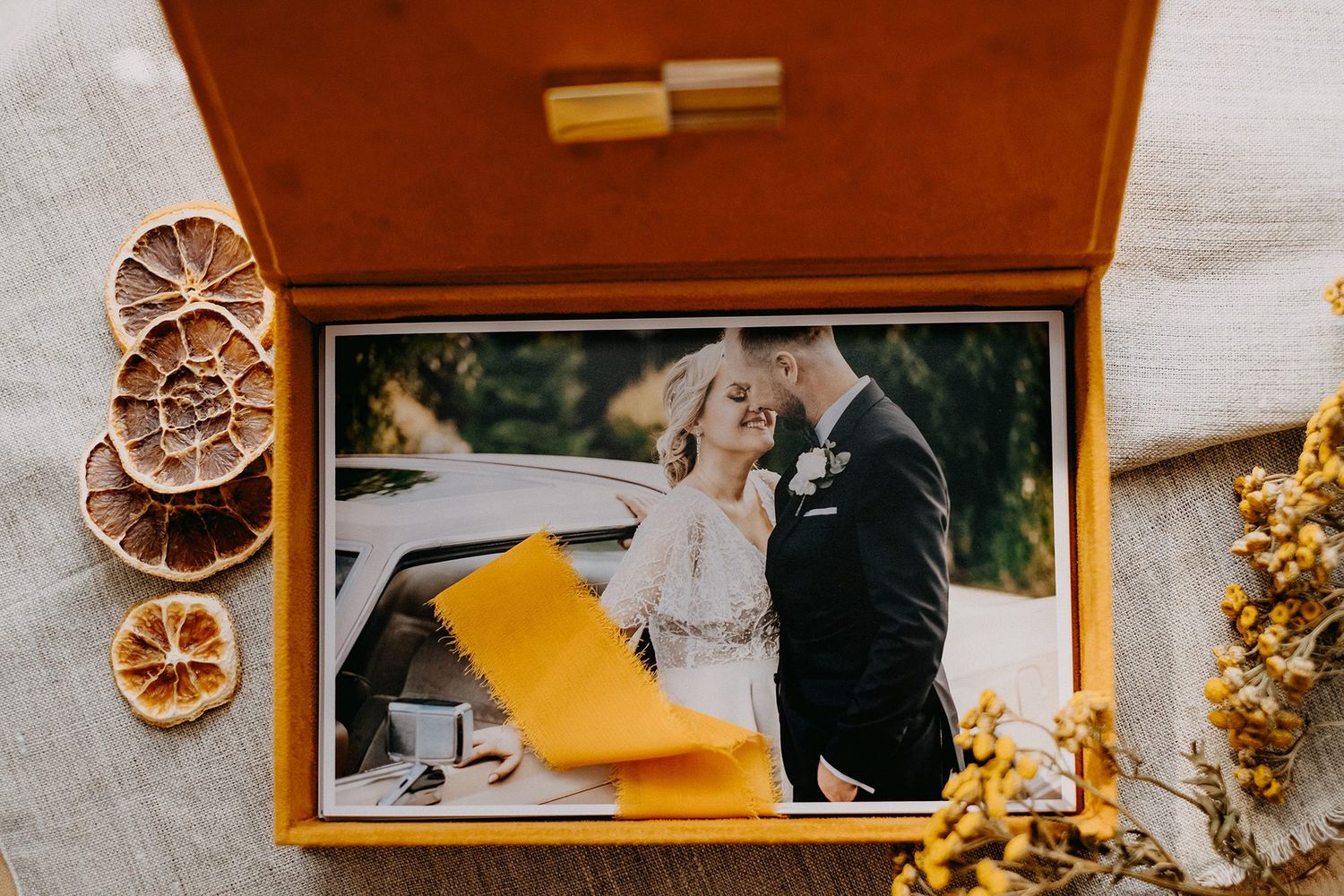 Warm wooden wedding photo box open displaying couple portrait with yellow ribbon and dried flowers.