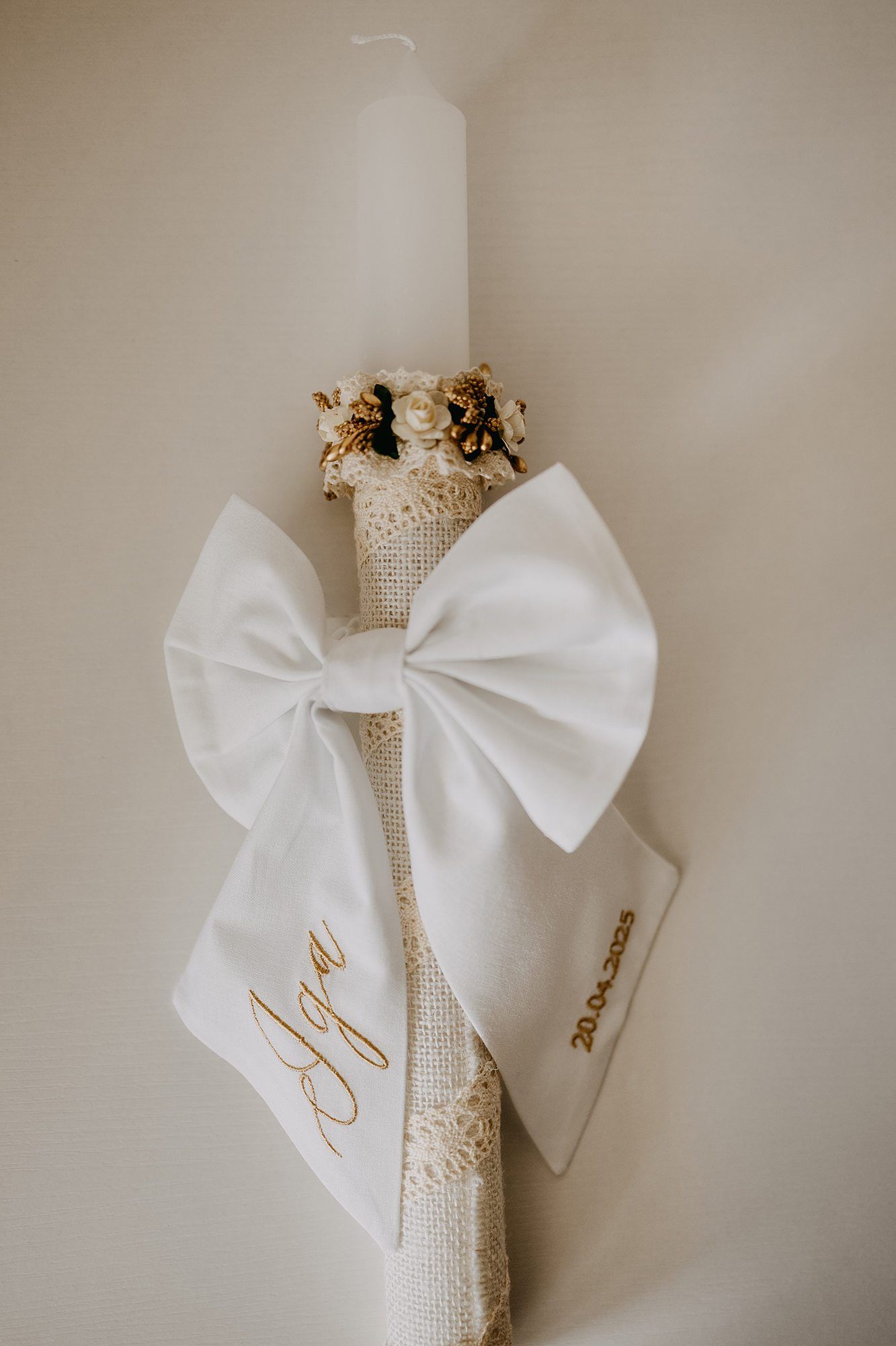 Elegant white christening candle decorated with satin bow, dried flowers, and gold script name.