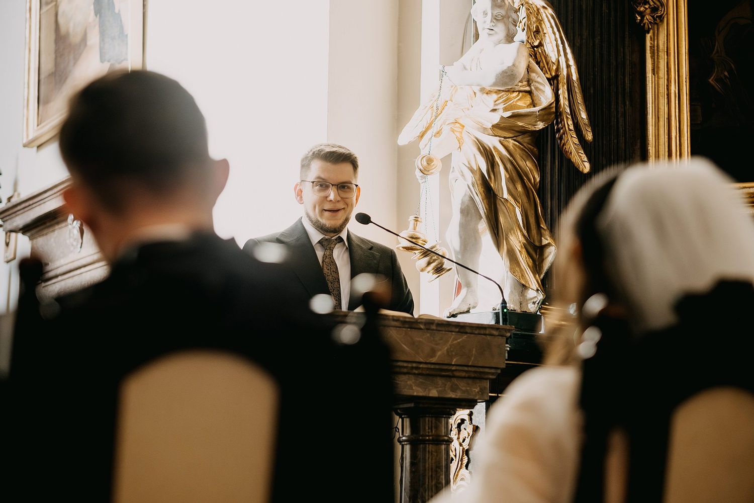 Wedding officiant speaks at podium before bride and groom during elegant church wedding ceremony.