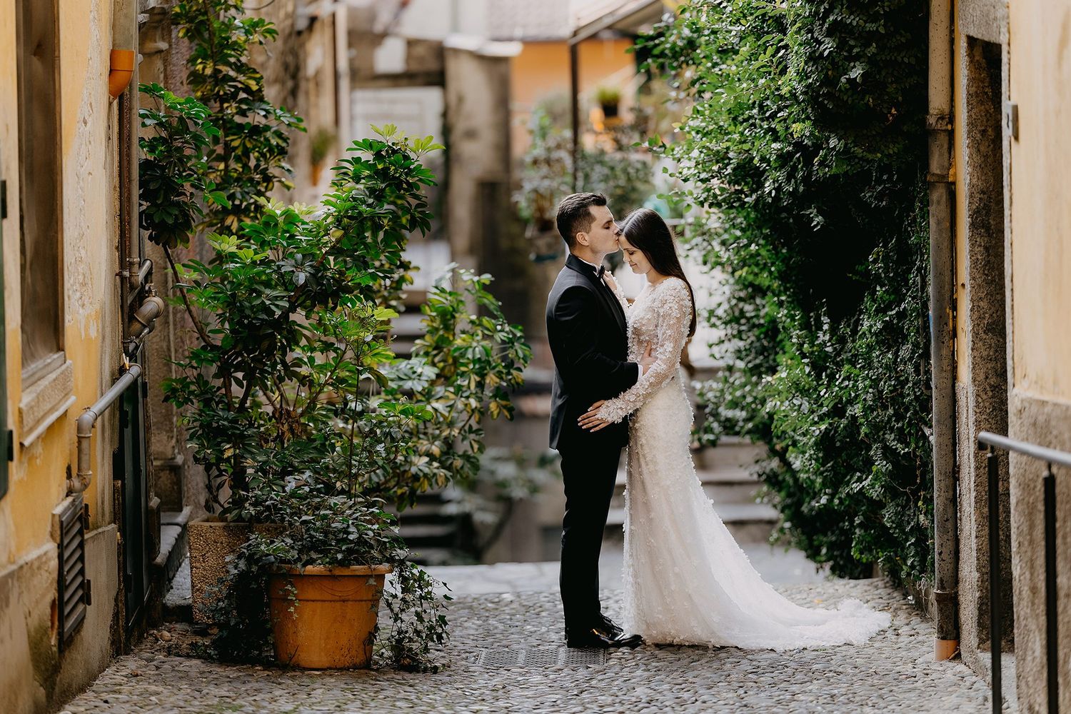 Bride and groom share intimate moment in charming ivy-lined Italian cobblestone alleyway.