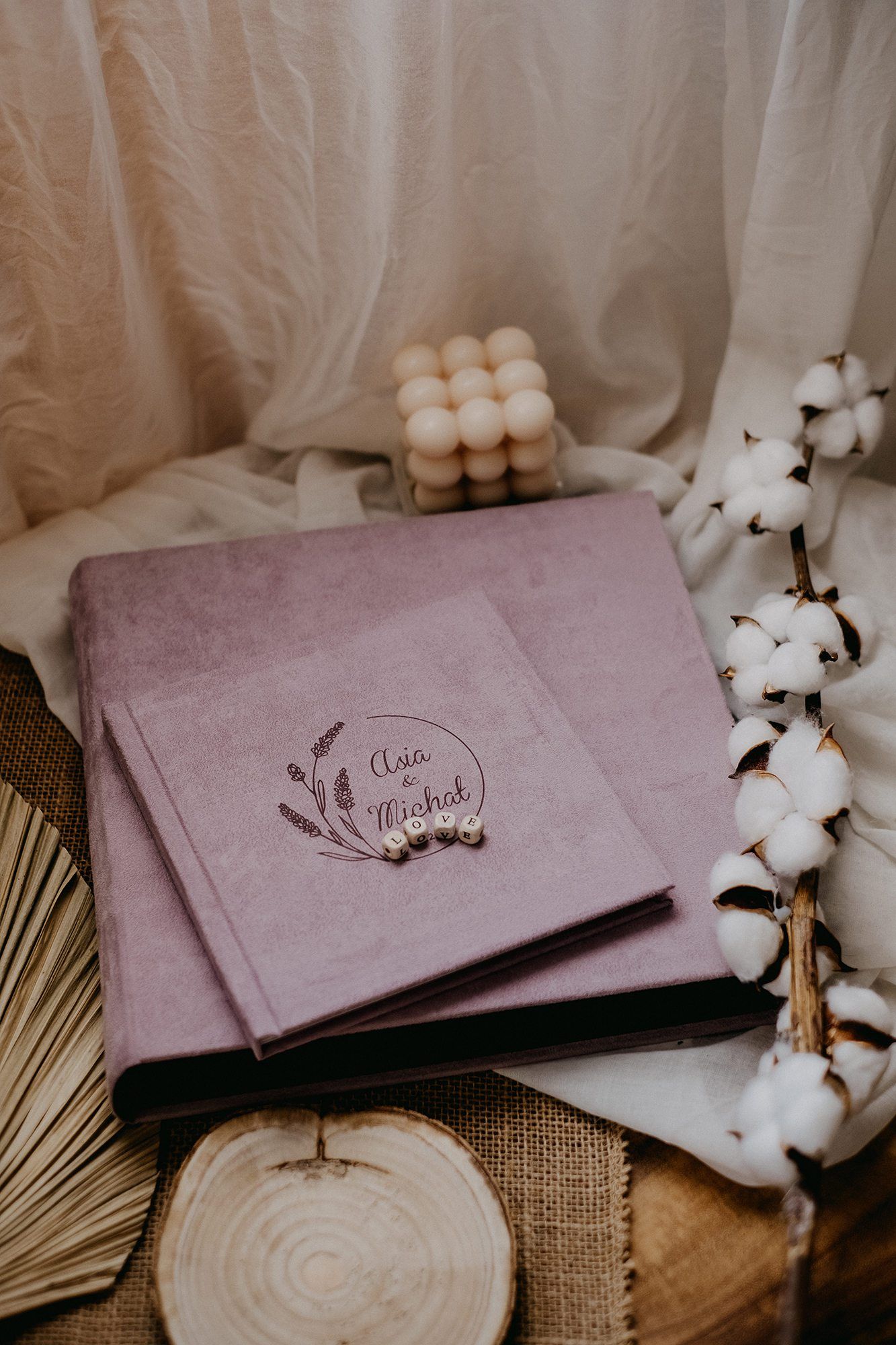 Pink velvet wedding photo album with floral embroidery beside cotton branches and candle.