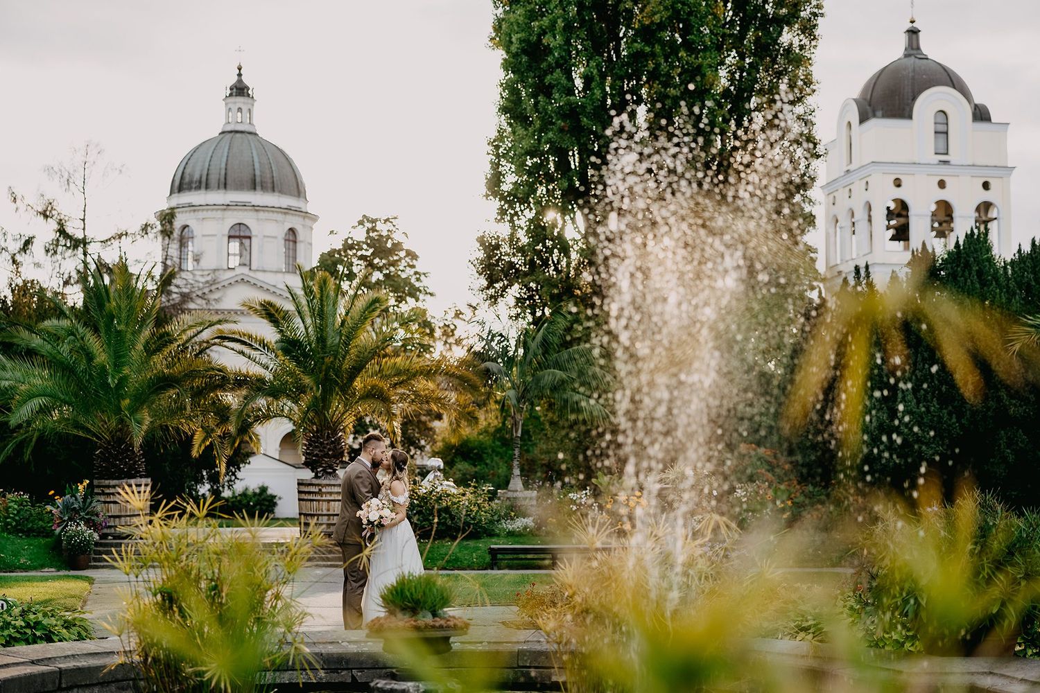 Bride and groom sharing a romantic moment near a fountain with a domed church in the background.