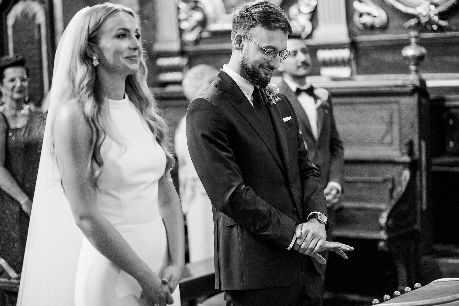 Black and white photo of bride and groom holding hands at altar.