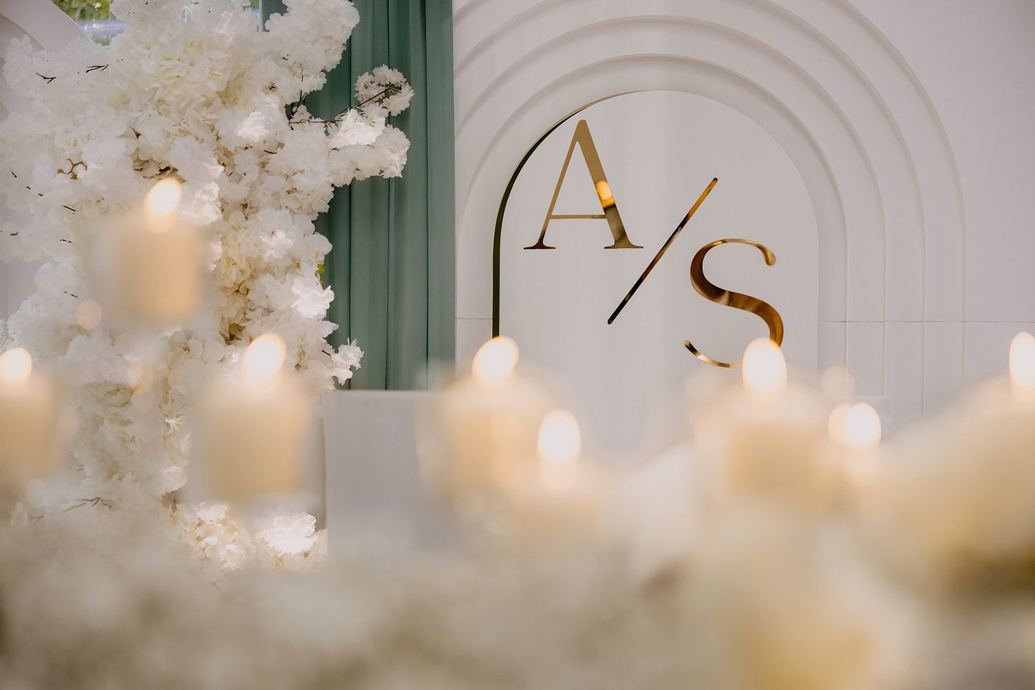 Elegant wedding backdrop featuring gold AS monogram initials, white floral arrangements, and glowing candles.